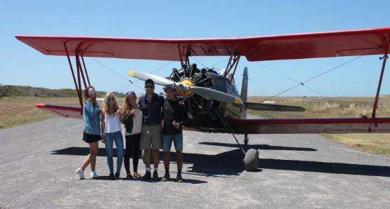 Visitors standing beside a red vintage biplane on an airfield