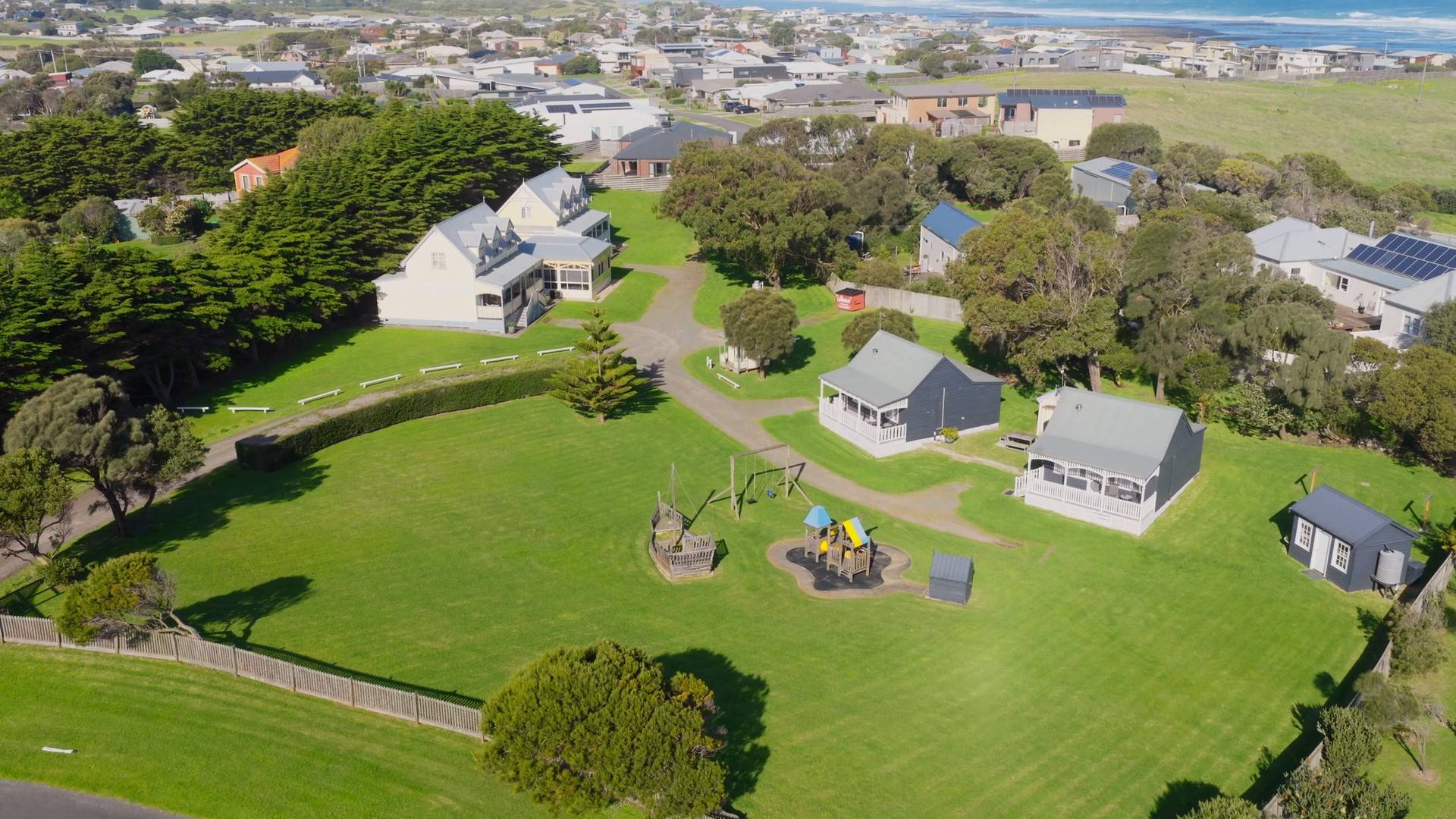 Aerial view of the Ocean Ridge Retreat grounds: grey villas, playgrounds and lawns ringed by trees