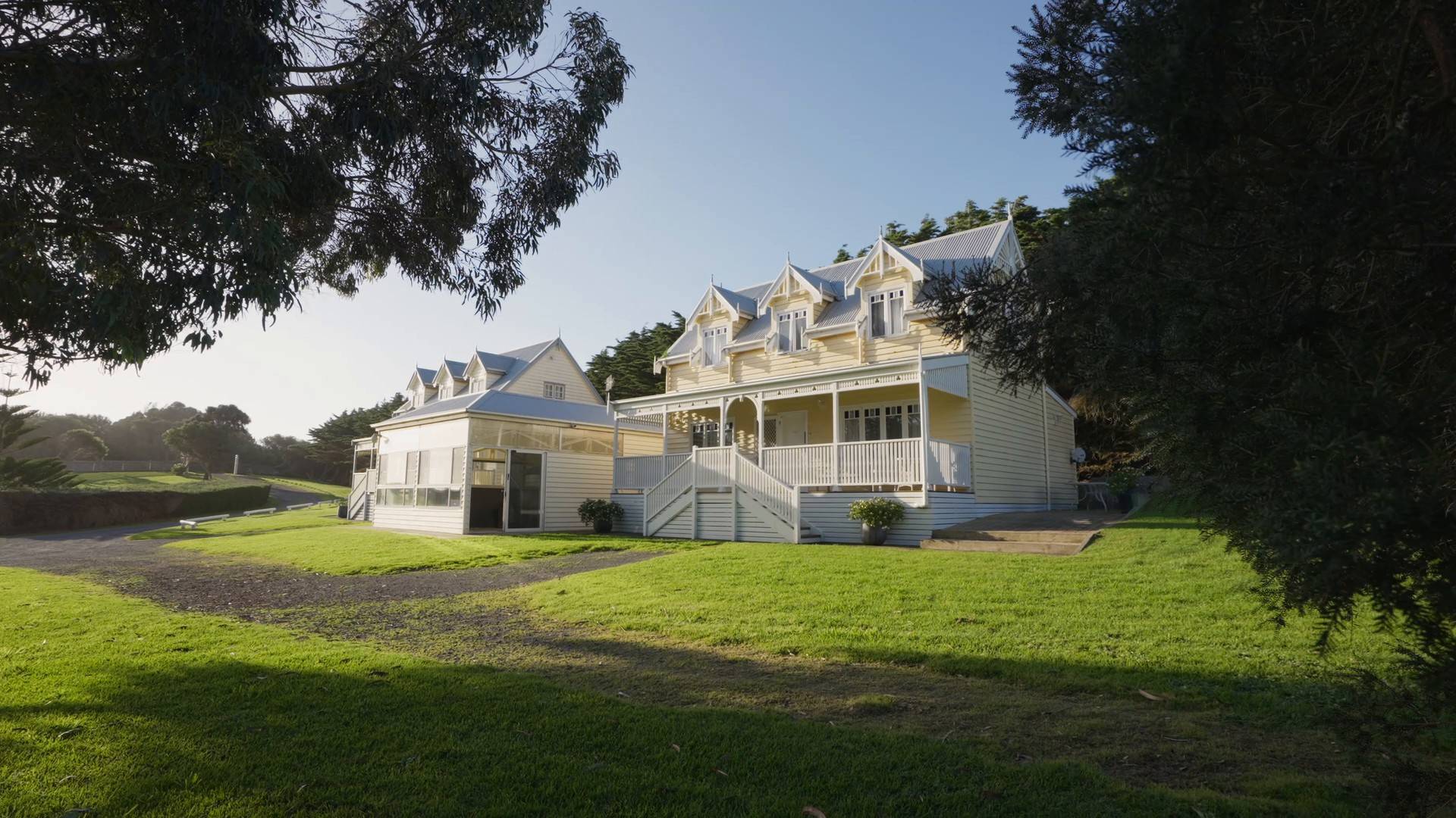 Dunes villa seen across the lawn, a cream two-storey home with gabled roof and verandah framed by trees