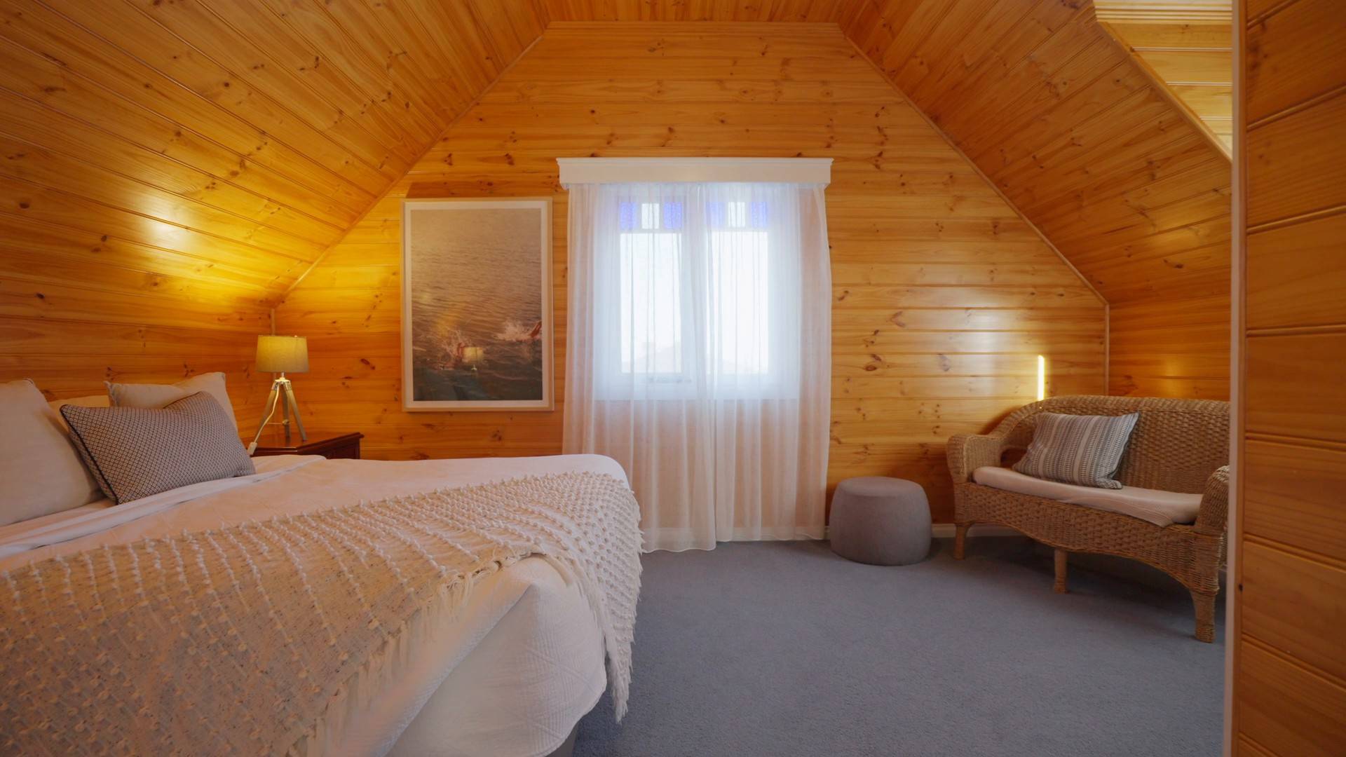 Upstairs bedroom in the Dunes villa with timber-lined walls, a queen bed and a two-seater couch