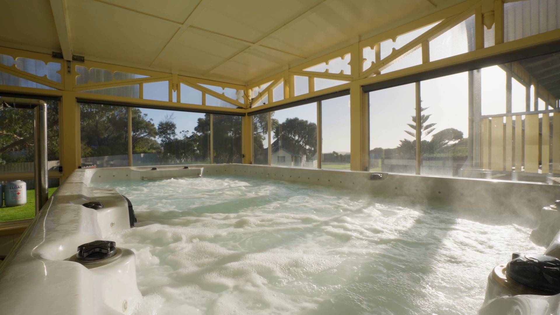Heated indoor swim spa with bubbling water under a timber-framed glass enclosure