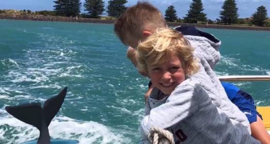 Child on a Mulloka cruise boat with a whale tail in the sea behind
