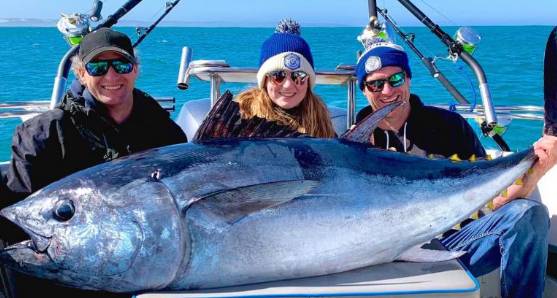 Fishing charter guests holding a large tuna on deck