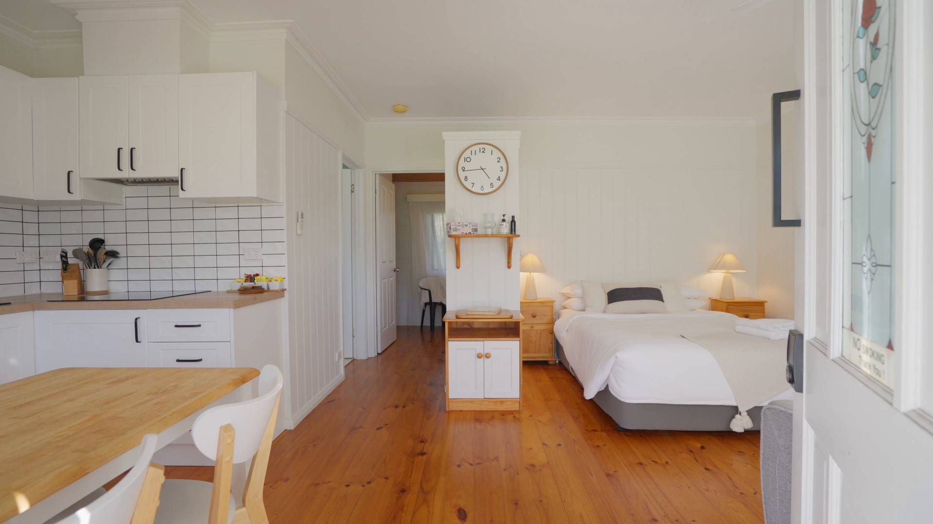 Bright villa interior with timber floors, kitchenette and a made-up bed beyond