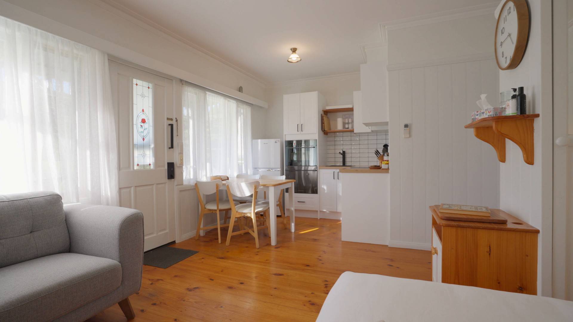 Villa living area with grey couch, timber floors and kitchen with dining table