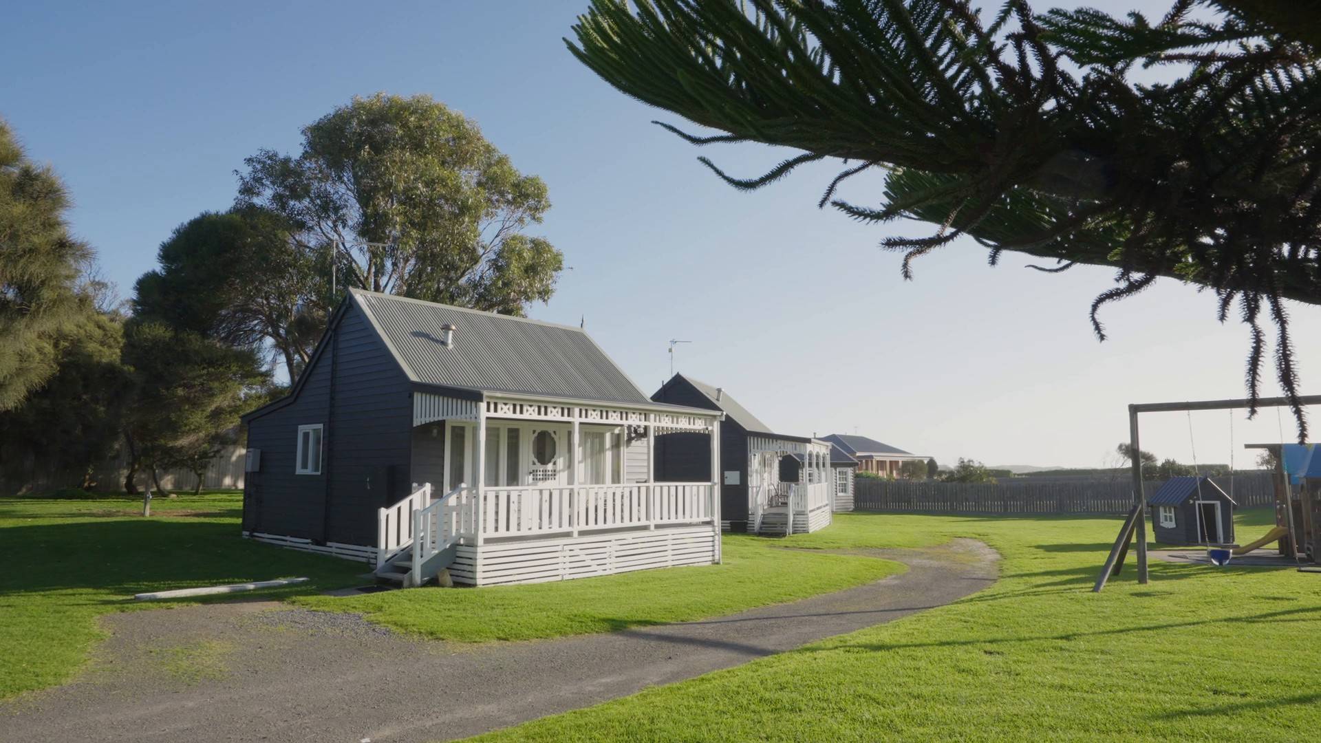 Grey weatherboard villa with white verandah on a wide lawn under Norfolk Island pines